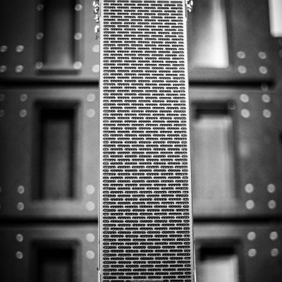 Colunas acústicas pretas metálicas com marca OKUNKA e parede preta ao fundo