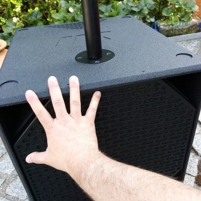 Coluna de som preta com grelha perfurada e mão aberta apoiada