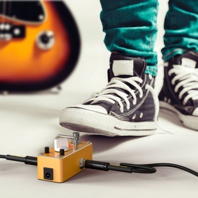 Pedal de efeitos amarelo junto a ténis pretos e guitarra laranja