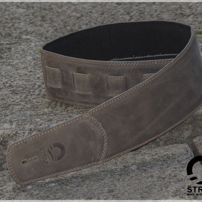 Cinta de guitarra de couro castanha escura com logo STRAP sobre pedra cinzenta
