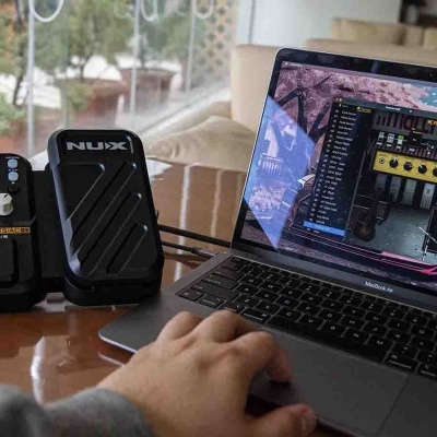 Pedal multiefectos NUX CG-2 e pedal de expressão NUX ao lado de computador portátil num ambiente interior com janela