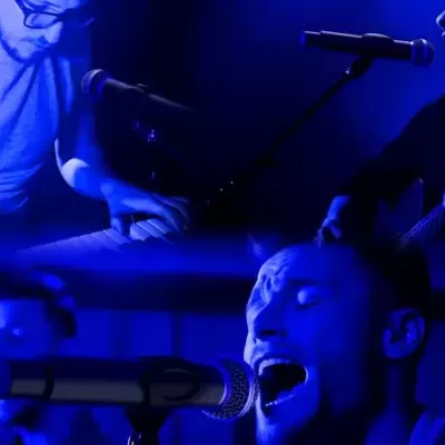 Três músicos em palco com instrumentos e microfones sob luz azul