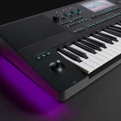 Teclado musical eletrónico preto com ecrã e botões coloridos numa mesa preta