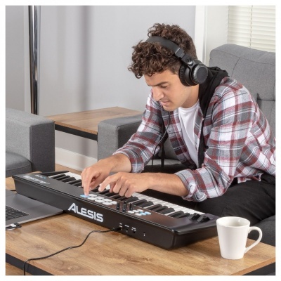 Teclado controlador MIDI Alesis numa mesa com jovem usando auscultadores