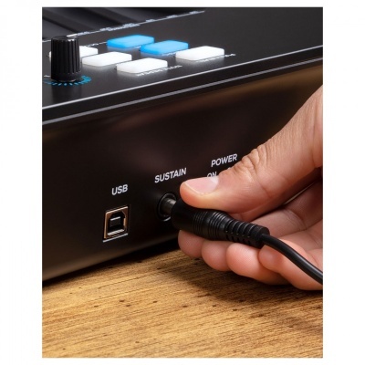 Mão a ligar cabo em equipamento preto com botões brancos e azuis sobre mesa de madeira