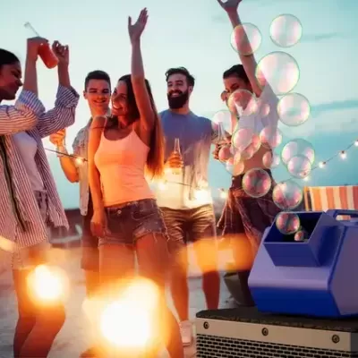 Máquina de bolhas azul a produzir bolhas com grupo de jovens a festejar ao entardecer