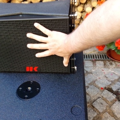 Caixa acústica preta com textura quadriculada e logótipo vermelho 'HK'