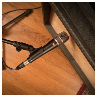 Microfone preto com suporte ajustável próximo a amplificador em piso de madeira.