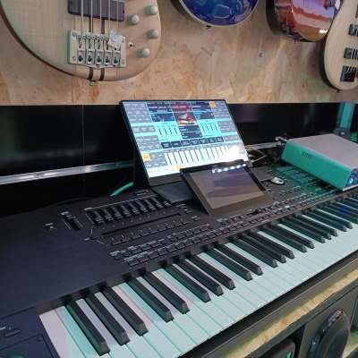 Teclado musical preto com ecrã tátil e monitor, com guitarras elétricas na parede de fundo