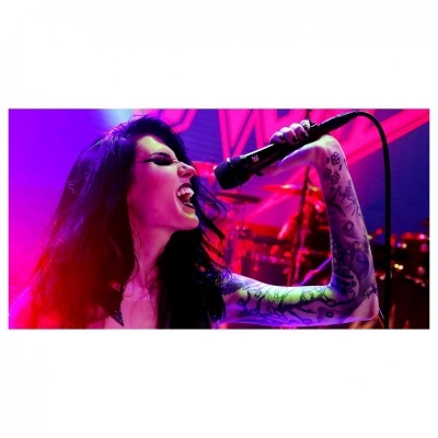 Cantora a segurar microfone com tatuagens num concerto com luzes coloridas