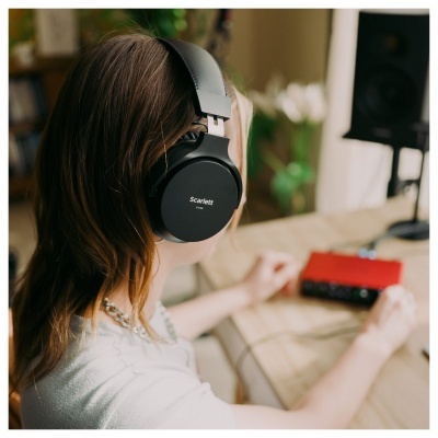 Pessoa com auscultadores pretos Scarlett sentada numa mesa com equipamento áudio vermelho