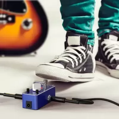 Pedais de efeito azul com sapatos pretos estilo converse e calças verdes junto a guitarra elétrica