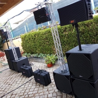 Equipamento de som profissional preto em ambiente exterior com piso de pedra e plantas