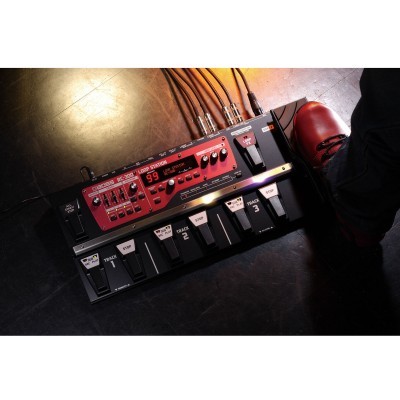 Pedaleira de guitarra vermelha com múltiplos botões e pedais num chão escuro