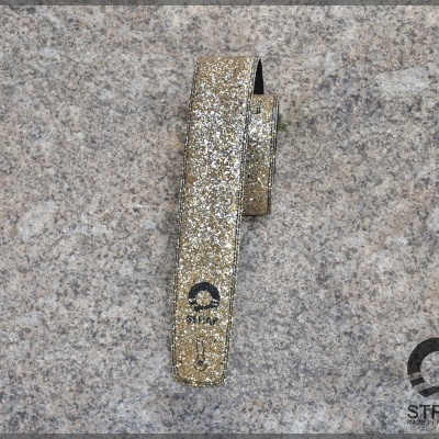 Correia para relógio dourada brilhante com texto Q STRAP sobre pedra cinzenta