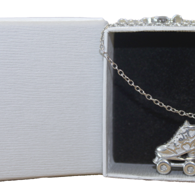 Colar prateado com pendente de patins numa caixa de joias branca.