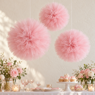 Três pompons cor-de-rosa de tule suspensos em ambiente decorado com flores e cupcakes