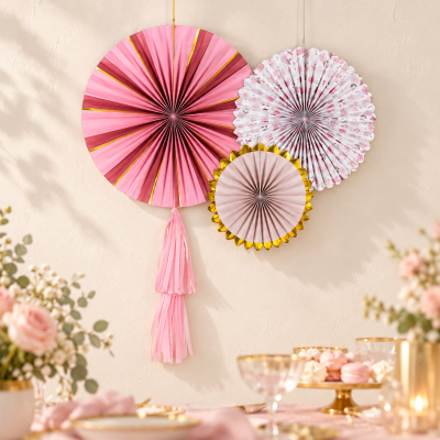 Decorações penduradas de papel rosa, branco e dourado numa parede bege sobre mesa decorada.