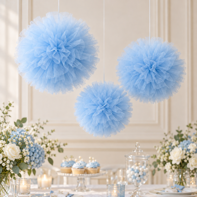 Pompons azuis de tule pendurados sobre mesa decorada com flores, cupcakes, velas e frasco com bolinhas.