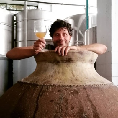 Ânfora de barro grande com pessoa segurando copo de vidro com líquido amarelo em ambiente industrial