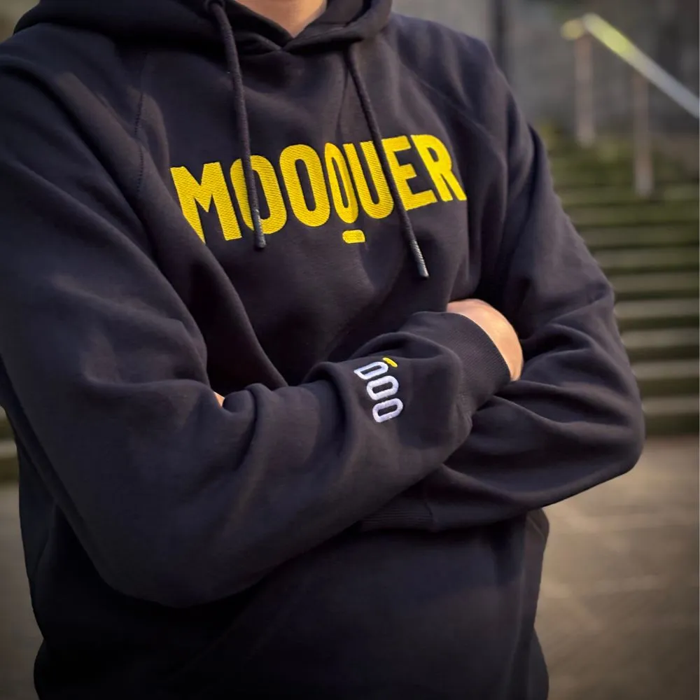Sweatshirt preta com texto amarelo MOOQUER no peito e palavra doo na manga