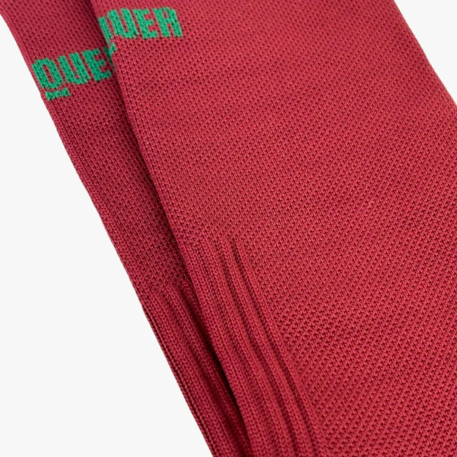 Meias vermelhas de malha com texto verde QUE no topo.
