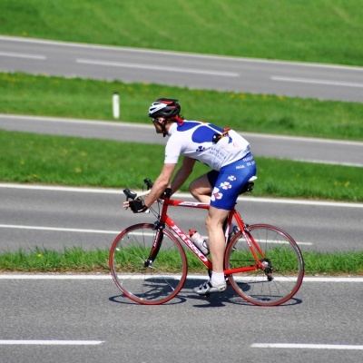 Ciclista em bicicleta de estrada vermelha numa estrada com relva verde ao fundo