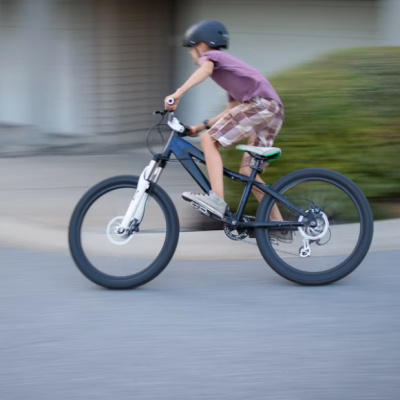 Criança a andar de bicicleta de montanha preta e branca com capacete num ambiente urbano