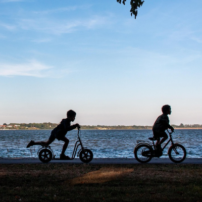 Crianças em bicicleta e trotinetes junto a um lago ao pôr do sol