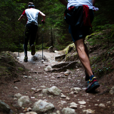 Dois homens em trilho de floresta com bastões de caminhada e roupa desportiva.