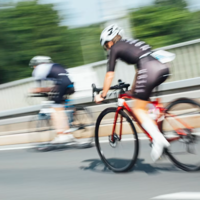 Duas bicicletas de estrada em movimento com ciclistas em roupa preta com capacetes brancos