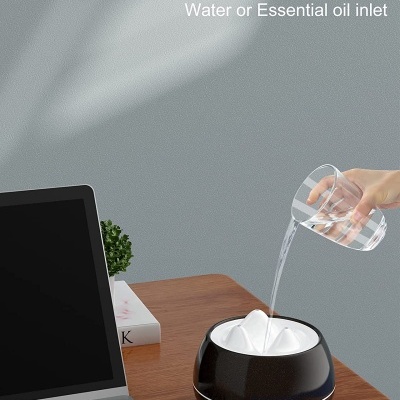 Difusor de aroma preto a ser enchido com água numa mesa ao lado de portátil