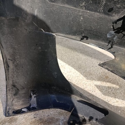 Para-choques automóvel preto danificado e sujo sobre superfície cinzenta