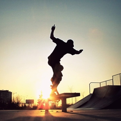 Pessoa a fazer manobra de skate em silhueta num skatepark ao pôr do sol