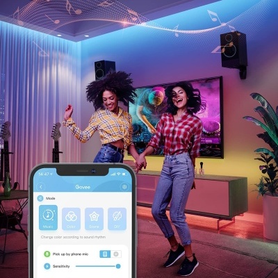 Duas mulheres a dançar numa sala com luzes LED coloridas e aplicação de controlo de luzes no smartphone