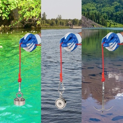Três anzóis magnéticos de pesca diferentes segurados por mãos com luvas azuis sobre água e paisagem natural
