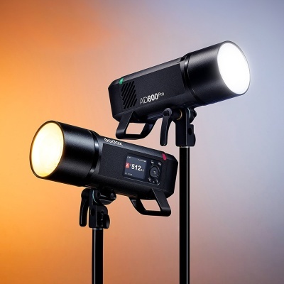Dois flashes Godox AD800Pro pretos em tripés com luz acesa, fundo degradê laranja cinza.