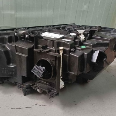 Peça automóvel preta complexa numa superfície cinzenta com parede e caixa ao fundo