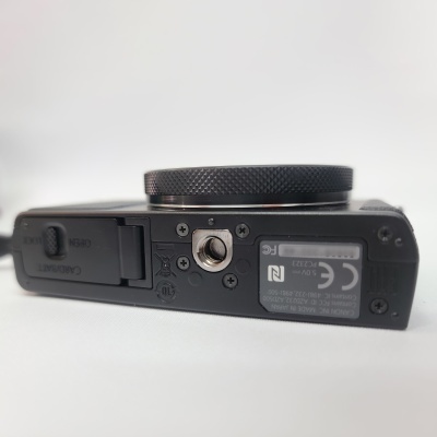 Base inferior de câmera digital preta com parafuso para tripé e etiquetas técnicas