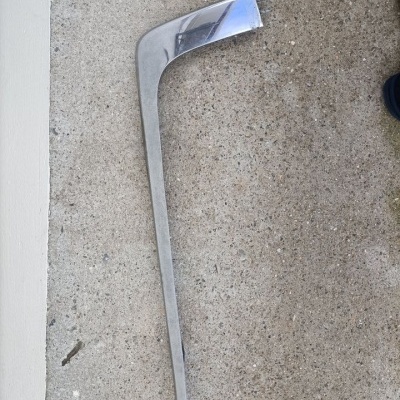 Peça metálica curva sobre chão de cimento junto a parede branca