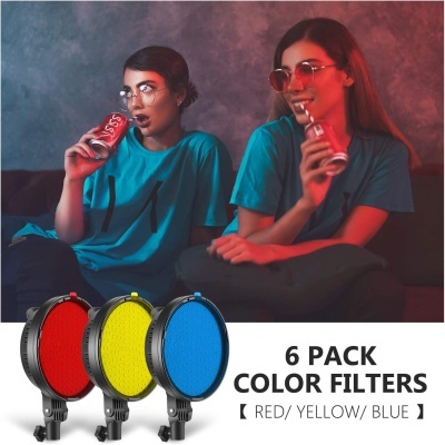 Duas mulheres de t-shirt azul bebem Coca-Cola sentadas em sofá com filtros coloridos de luz embaixo.