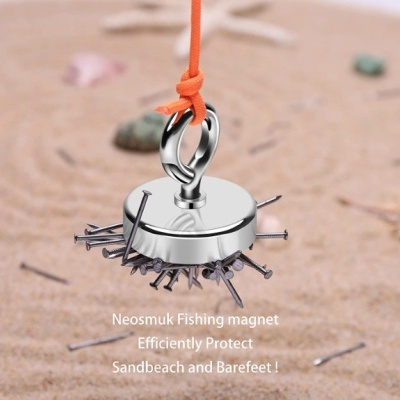 Íman de pesca prateado com pregos atraídos pendurado por cordão laranja sobre areia