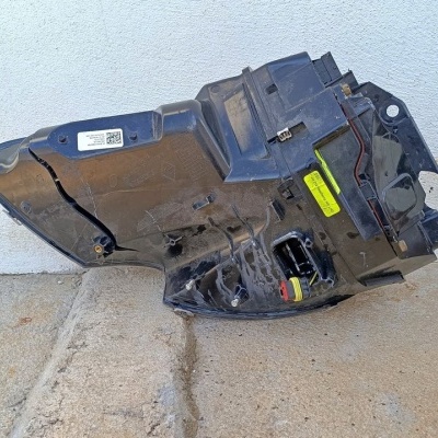 Peça automóvel preta com etiquetas e fiações no chão