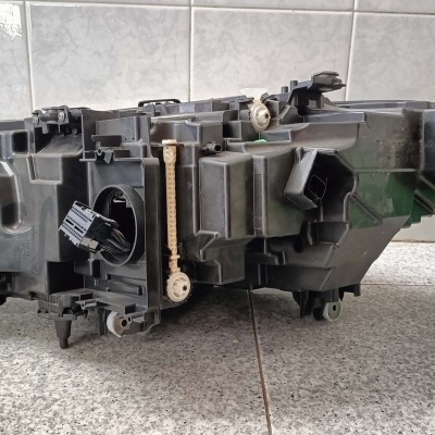 Farol dianteiro automóvel preto de plástico com componente interior cinza sobre chão de azulejo cinza