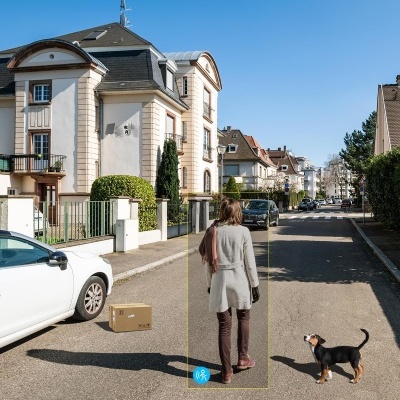 Rua residencial com pessoa e cachorro, caixa no chão e texto em espanhol no céu