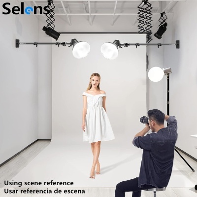Modelo vestida de branco em estúdio de fotografia com luzes suspensas e fotógrafo sentado