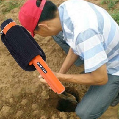 Detector de metais portátil laranja com capa preta e homem a cavar no solo ao fundo