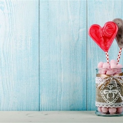 Frasco decorado com marshmallows e pirulitos em forma de coração sobre fundo azul claro