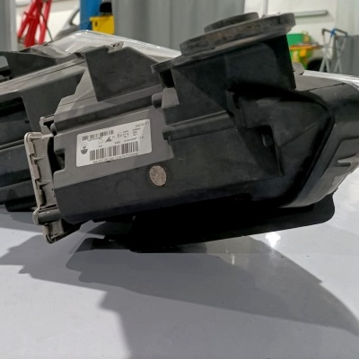 Unidade de farol automóvel com etiqueta e caixa preta numa superfície branca