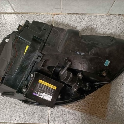 Peça automóvel preta de plástico com etiquetas numa superfície de azulejos cinzentos